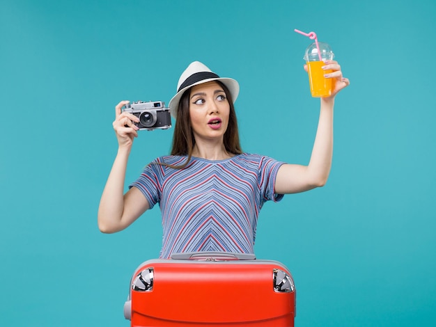 Donna di vista frontale in vacanza che tiene il succo e la macchina fotografica sulla vacanza di viaggio di viaggio di estate di viaggio del mare del fondo blu