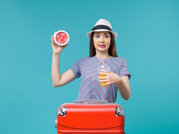 Front view woman in vacation holding juice and clock on a blue background voyage vacation sea trip journey