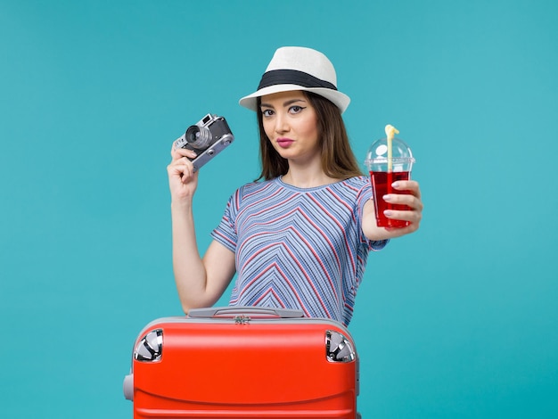 Front view woman in vacation holding juice with camera on blue background sea summer voyage plane journey