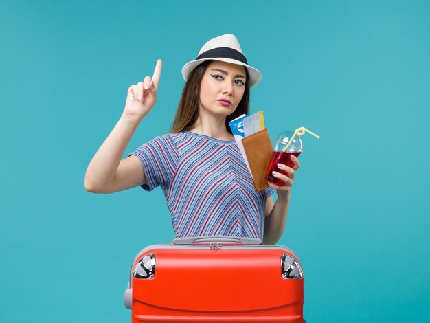 Front view woman in vacation holding juice with tickets on the blue background voyage female sea summer plane journey