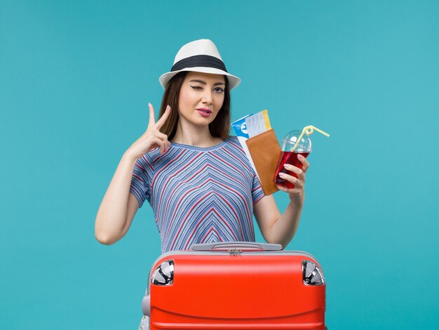 水色の背景の航海の旅の女性の海の夏の飛行機のチケットとジュースを保持している休暇中の正面図の女性