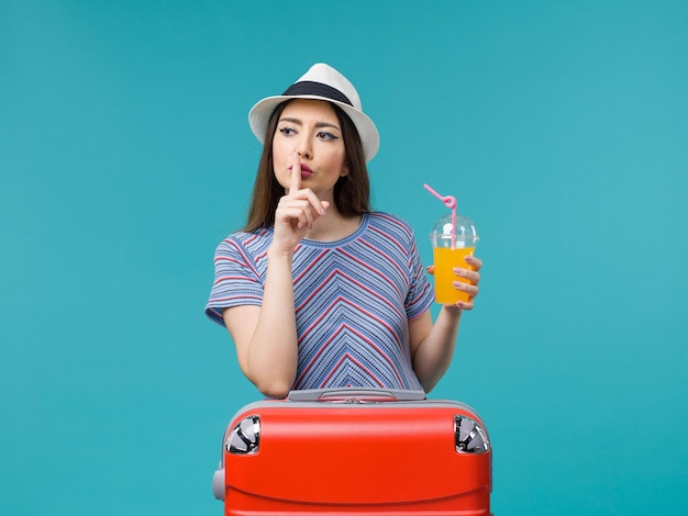 Front view woman in vacation with her red bag holding her juice on a light blue background trip journey voyage vacation female