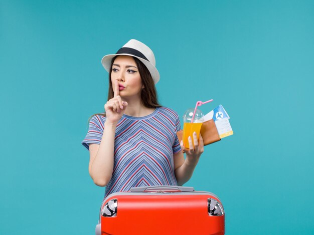 Front view woman in vacation with her red bag holding tickets and juice on the blue background journey voyage vacation female trip