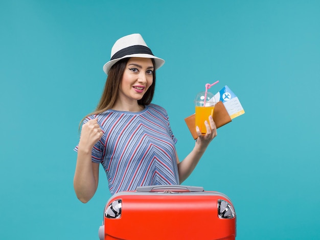 Вид спереди женщина в отпуске с ее красной сумкой, держащей билеты и сок на синем столе, поездка, путешествие, отпуск, женщина