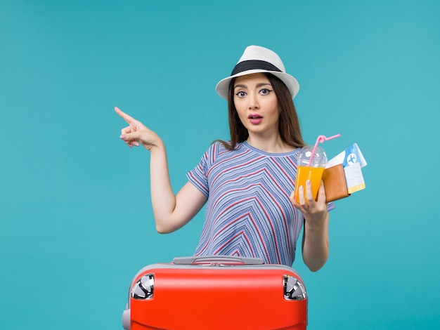 Front view woman in vacation with her red bag holding tickets and juice on blue desk journey voyage vacation female trip