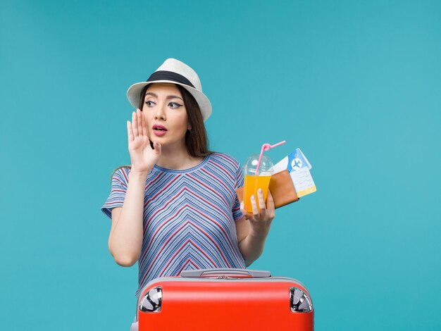 Front view woman in vacation with her red bag holding tickets and juice on blue floor journey voyage vacation female trip