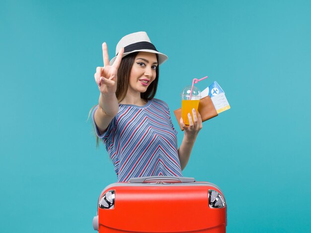 Вид спереди женщина в отпуске с ее красной сумкой, держащей билеты и сок на светло-синем фоне, путешествие, путешествие, отпуск, женщина