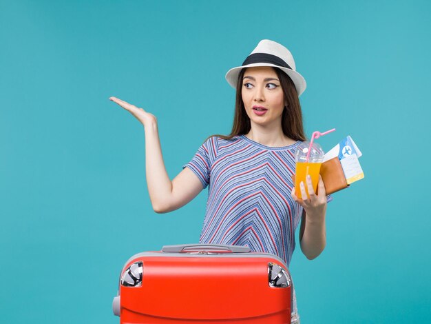 Front view woman in vacation with her red bag holding tickets and juice on light-blue background journey trip voyage vacation female