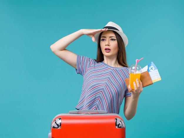 Front view woman in vacation with her red bag holding tickets and juice on light blue background journey voyage vacation female trip