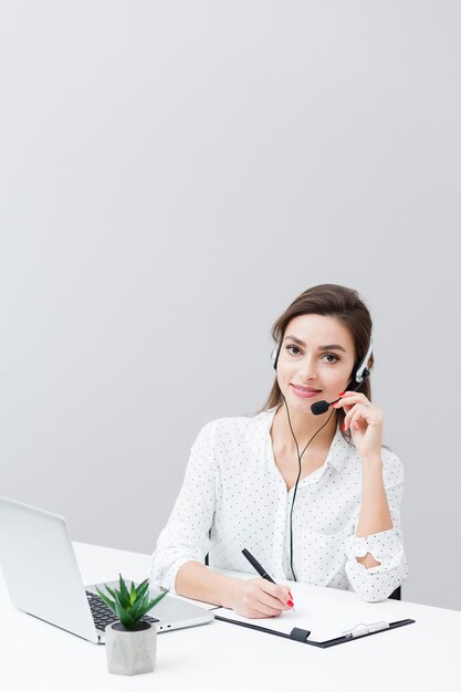 Front view of woman wearing headset and working at desk with laptop