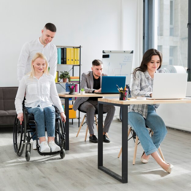 オフィスでの同僚によって助けられている車椅子の女性の正面図