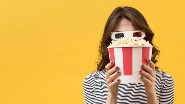 Front view woman with 3d glasses covering her face with a popcorn bucket