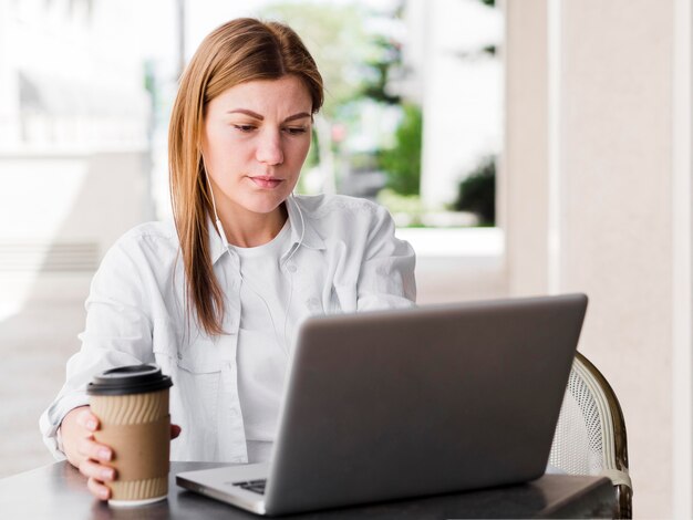 커피와 이어폰 야외에서 노트북에서 일하는 여자의 전면보기