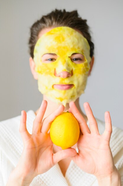 レモンを保持しているフェイスマスクを持つ女性の正面図