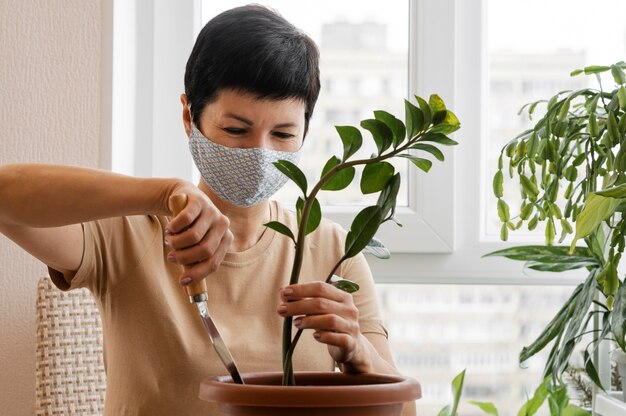 Вид спереди женщины с маской для лица, заботящейся о комнатном растении в горшке