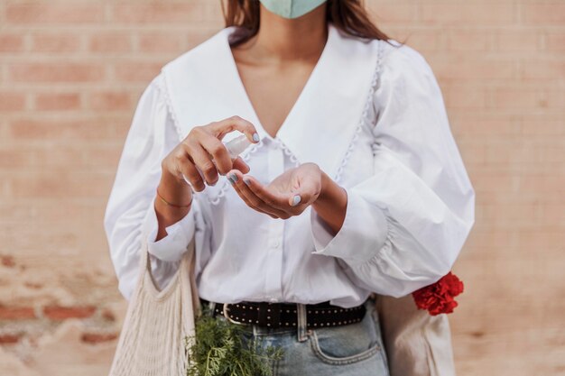 Front view of woman with face mask using hand sanitizer