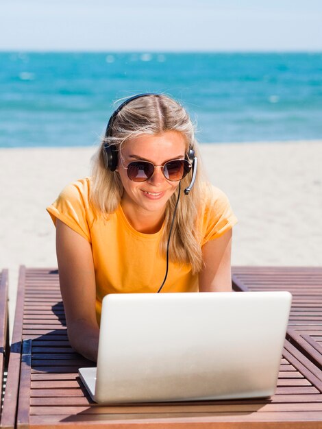 Front view of woman with headset and laptop working at the beach