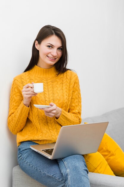 Вид спереди женщины с ноутбуком на коленях, держа чашку кофе