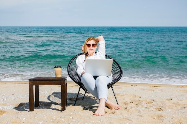 一杯のコーヒーとビーチで働くラップトップを持つ女性の正面図