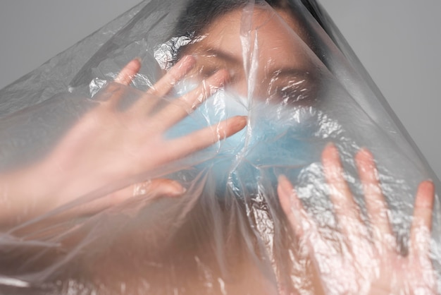 Front view woman with medical mask being covered in plastic