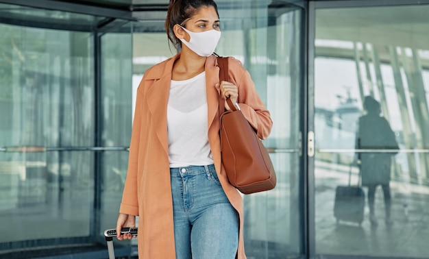 Foto gratuita vista frontale della donna con mascherina medica che trasportano bagagli all'aeroporto durante la pandemia