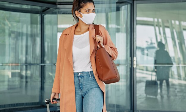 Front view of woman with medical mask carrying luggage at the airport during pandemic