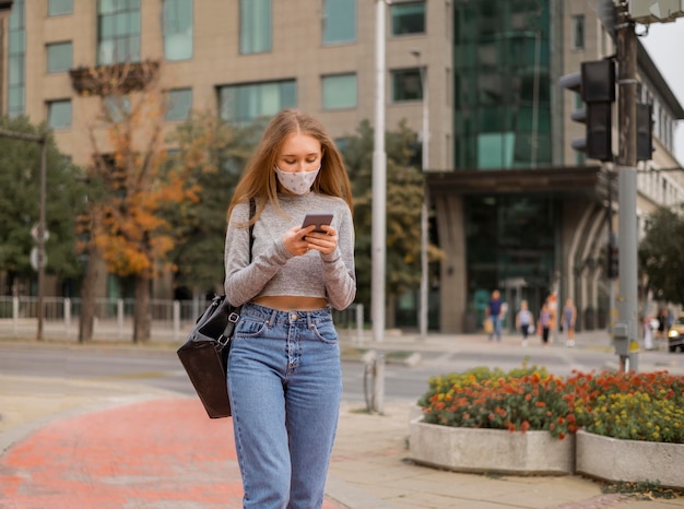 彼女の電話をチェックする医療マスクを持つ正面図の女性