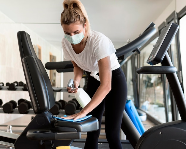 Front view of woman with medical mask cleaning gym equipment