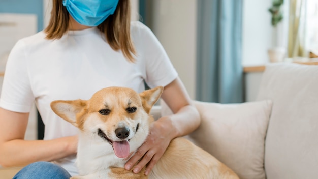 Вид спереди женщины с медицинской маской, ласки ее собаку на диване