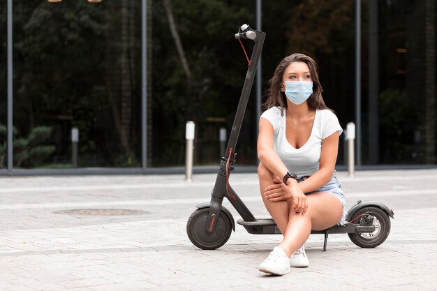 Front view of woman with medical mask sitting on electric scooter