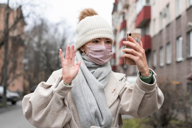 Front view of woman with medical mask waving at smartphone