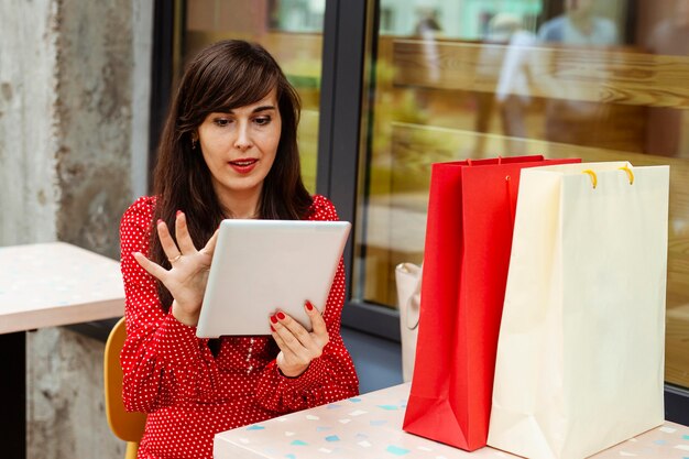 Front view of woman with shopping bags ordering items on sale using tablet