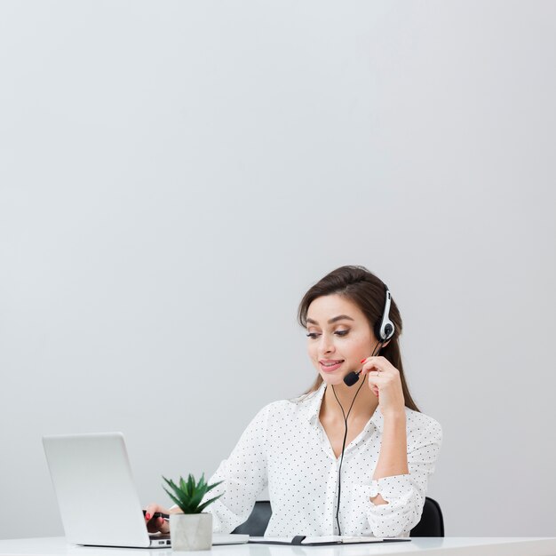 Front view of woman working at desk while wearing headset and looking at laptop