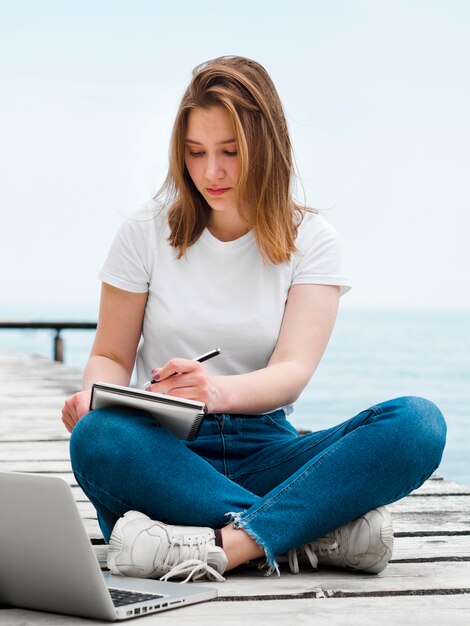 Вид спереди женщины, работающей на ноутбуке снаружи на пирсе