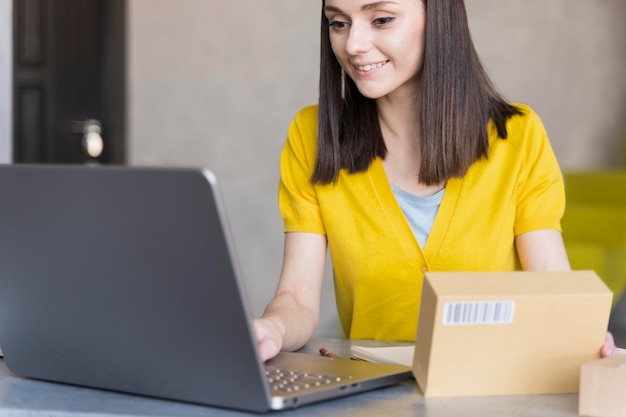 Front view of woman working on laptop while holding box
