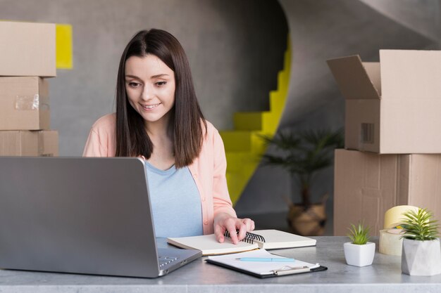 Front view of woman working on laptop with boxes in the back