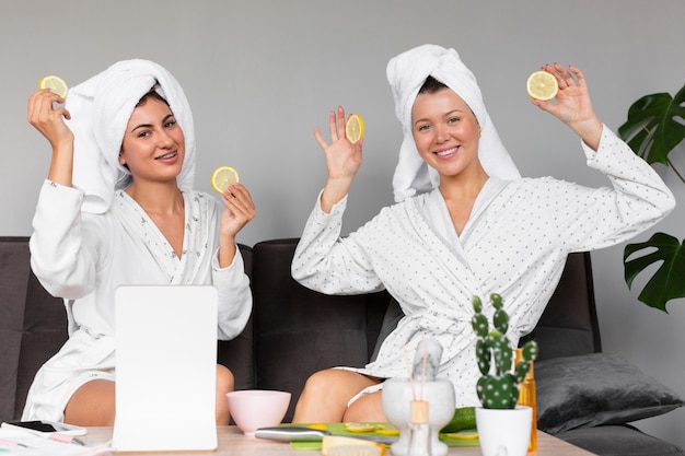 Free photo front view of women in bathrobes and towels holding lemon slices