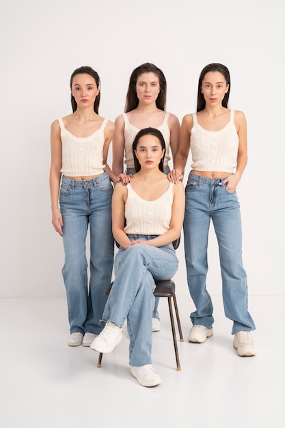 Вид спереди на женщин в майках и джинсах, позирующих со стулом на минималистских портретах
