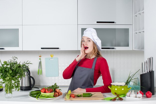 Front view wondered female cook in apron standing behind kitchen table