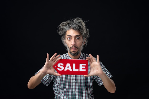 Free photo front view of wondered man holding sale sign on dark wall