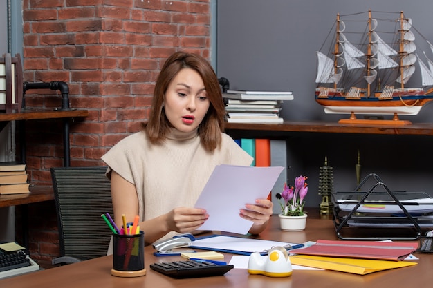 Front view of wondered woman checking papers sitting at office