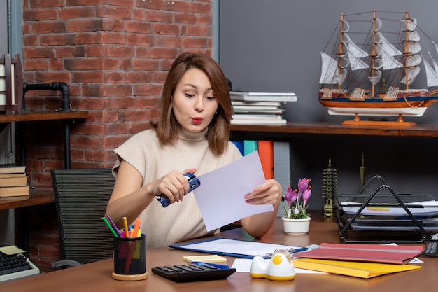 Free photo front view of wondered woman using stapler sitting at office