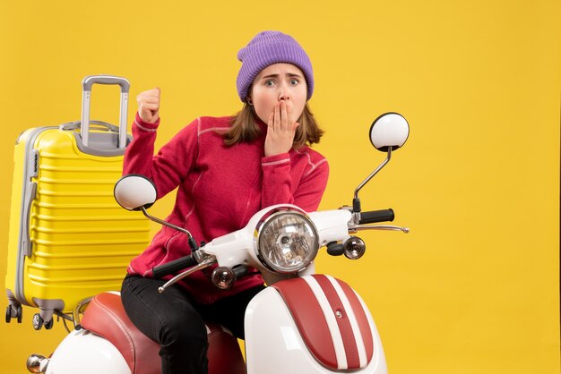 Front view wondered young girl on moped pointing at her suitcase