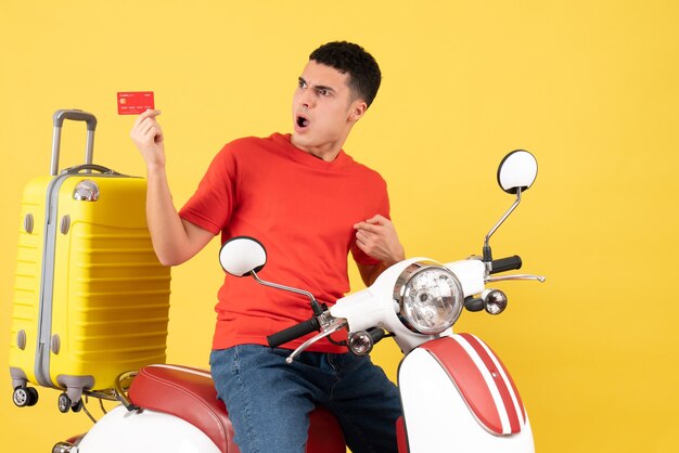 Front view wondered young man on moped holding discount card