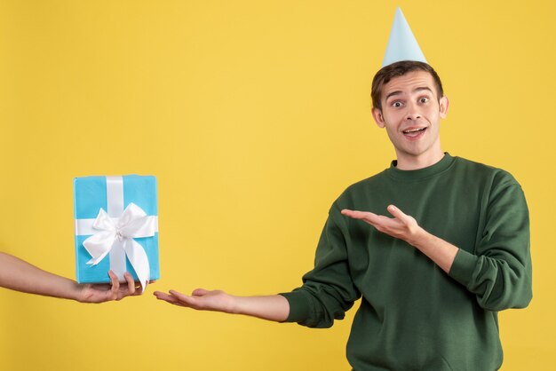Вид спереди удивился молодой человек, указывая на подарок в человеческой руке на желтом