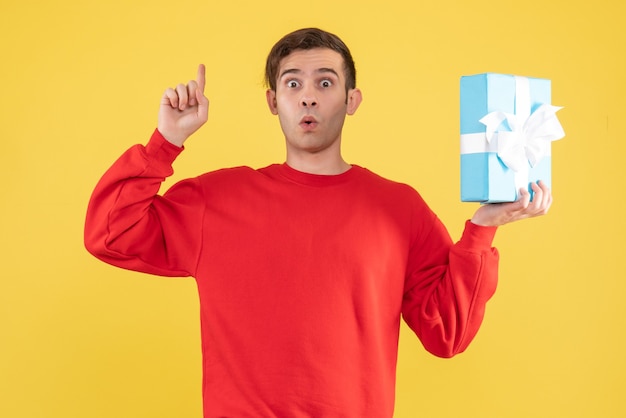 Front view wondered young man with red sweater finger pointing ceiling on yellow 