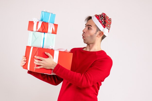 Вид спереди удивился молодой человек в новогодней шапке, глядя на подарки на белом