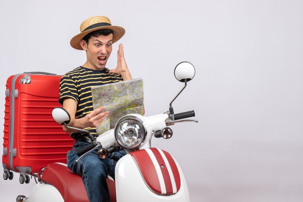 Вид спереди удивленного молодого человека в соломенной шляпе на мопеде, смотрящего на карту