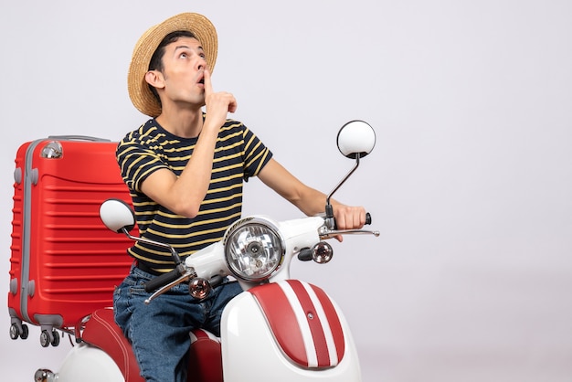 Front view of wondered young man with straw hat on moped making hush sign