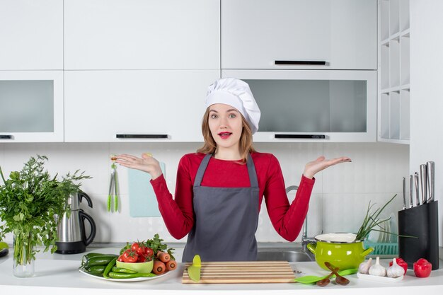 Front view wondered young woman in apron standing behind table